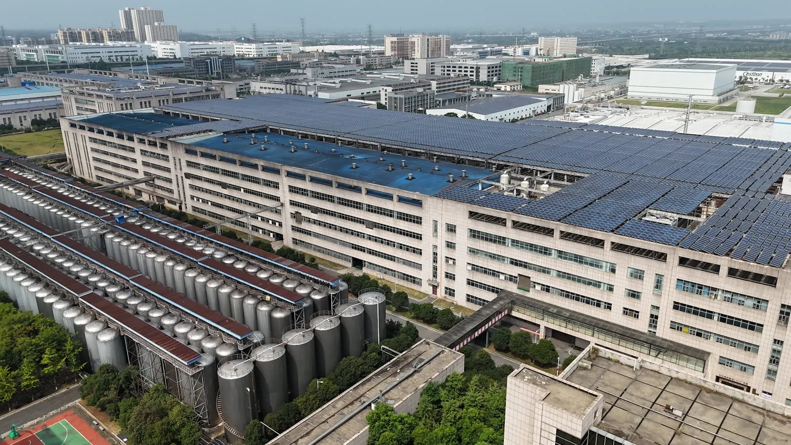 Aerial view of a commercial and industrial facility with rooftop photovoltaic arrays and adjacent storage tanks — the behind-the-meter site Entogo serves with industrial liquid-cooled BESS cabinets for peak shaving, time-of-use shifting and backup