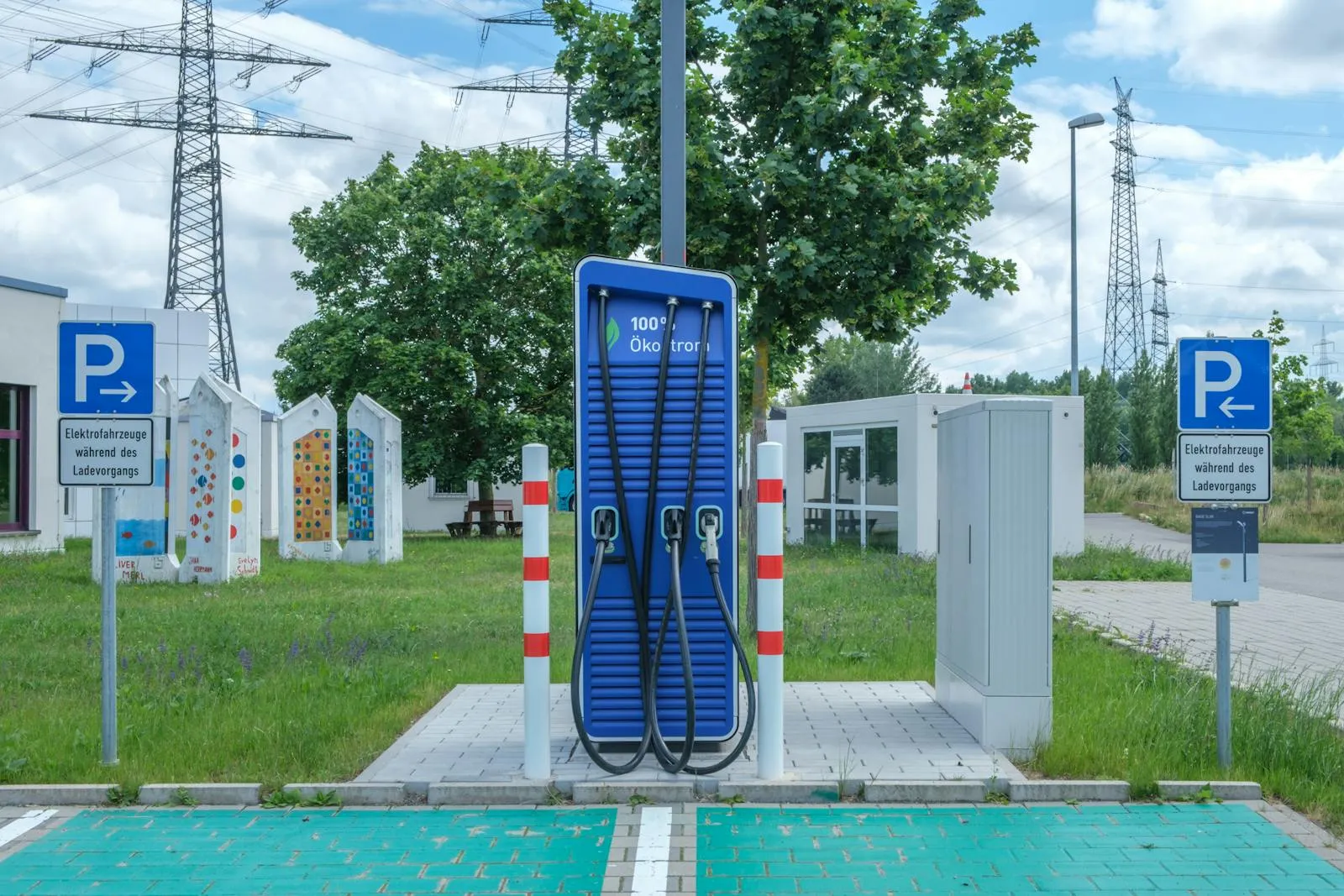Public DC fast electric-vehicle charging station with dual cables, marked EV parking bay and high-voltage transmission towers in the background — the public-network charging environment Entogo deploys AC and DC chargers into across North America